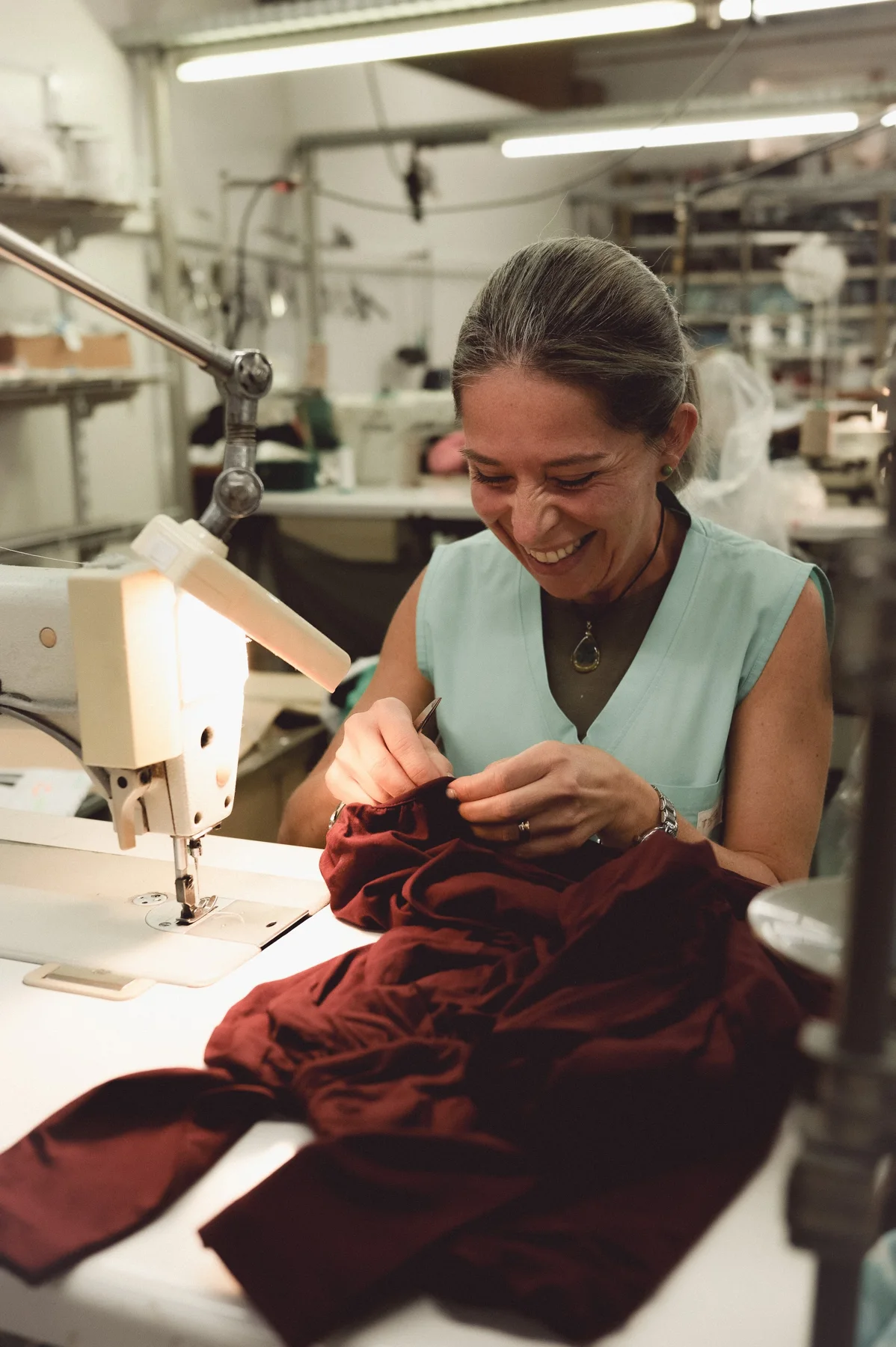 A garment maker working with burgundy fabric at a sewing machine in Portugal